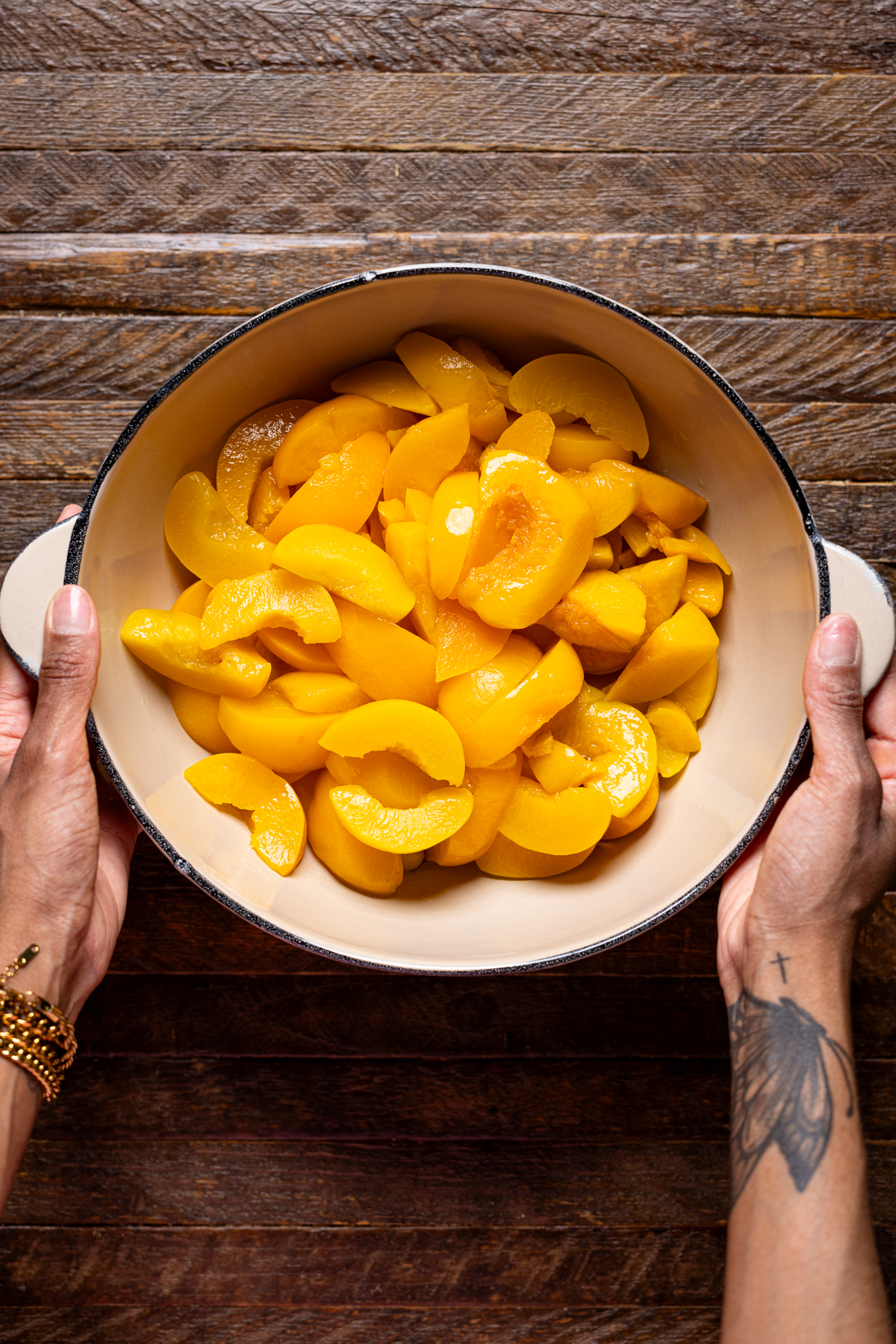 Image of a bowl of drained peaches in a bowl being held by hands.