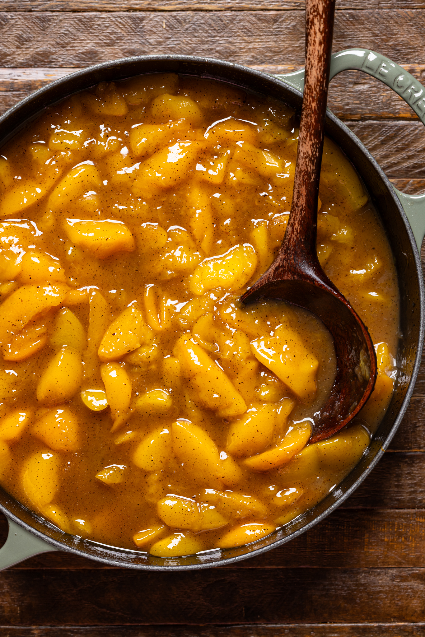Image of cooked peaches in a skillet with a wooden spoon.