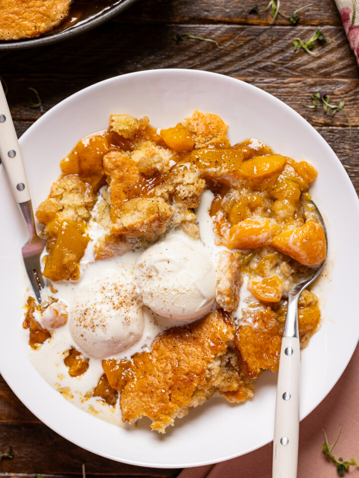 Up close shot of peach cobbler in a low bowl with scoops of ice cream.