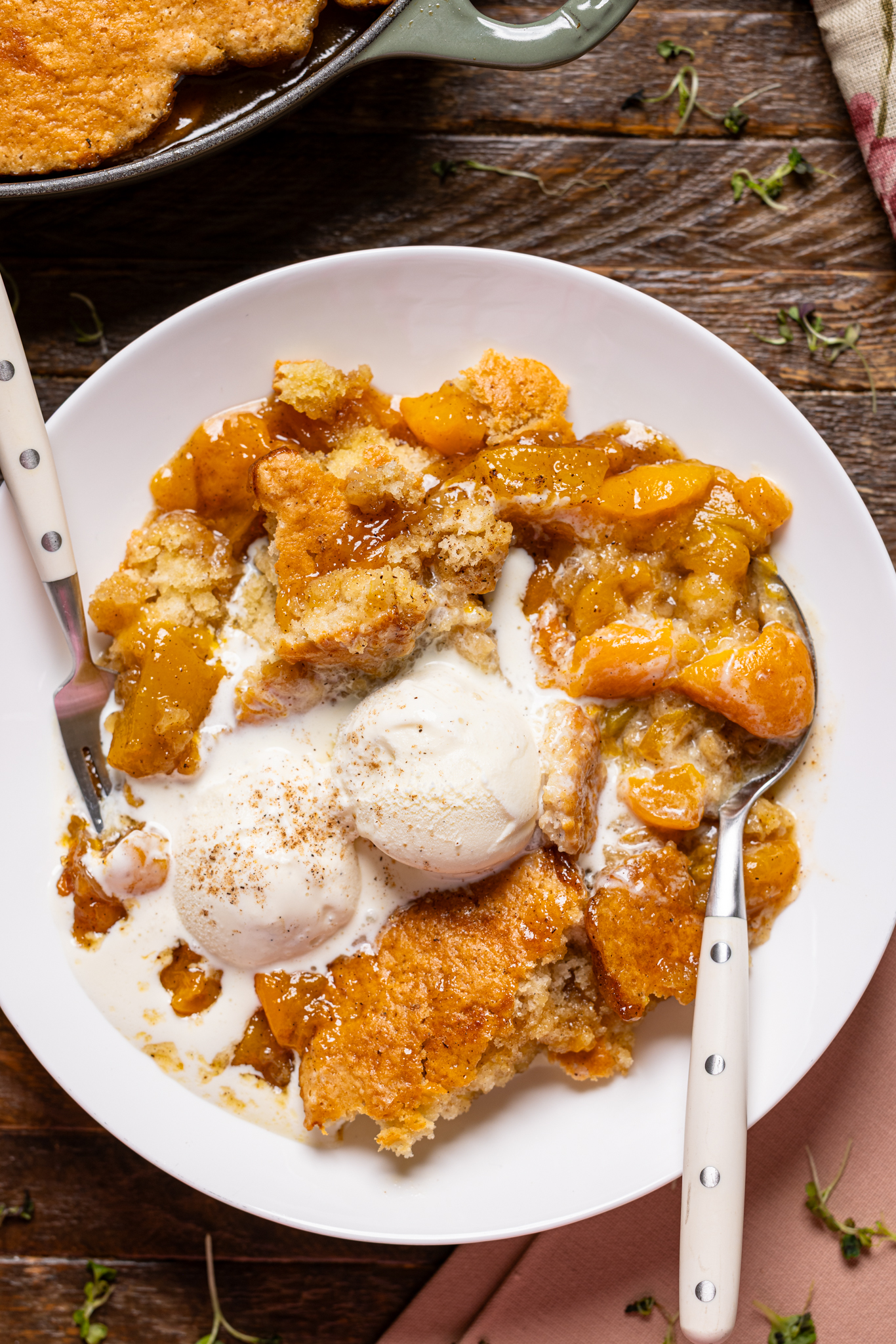 Up close shot of peach cobbler in a low bowl with scoops of ice cream.