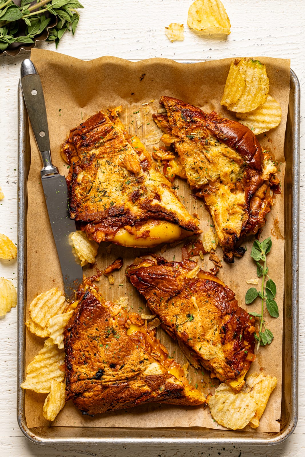 Grilled cheese sandwiches on a baking sheet with parchment paper, a knife, and chips.