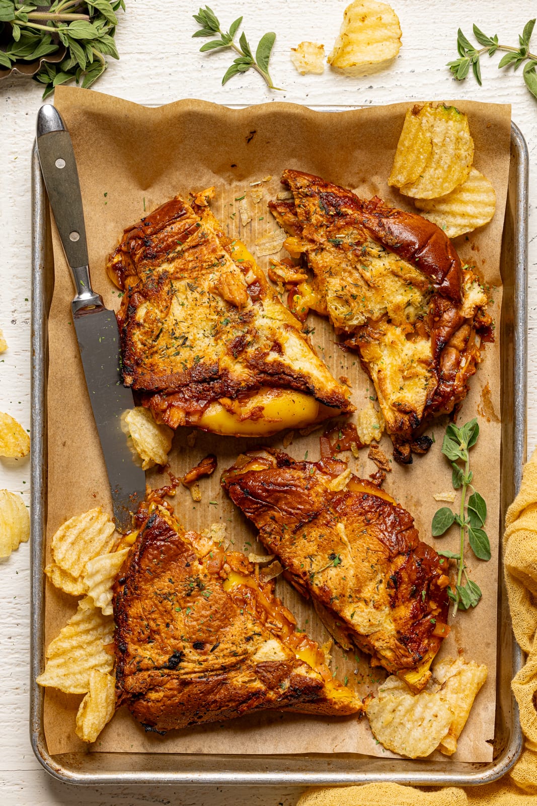 Sandwiches on a baking sheet with parchment paper with a knife and chips.