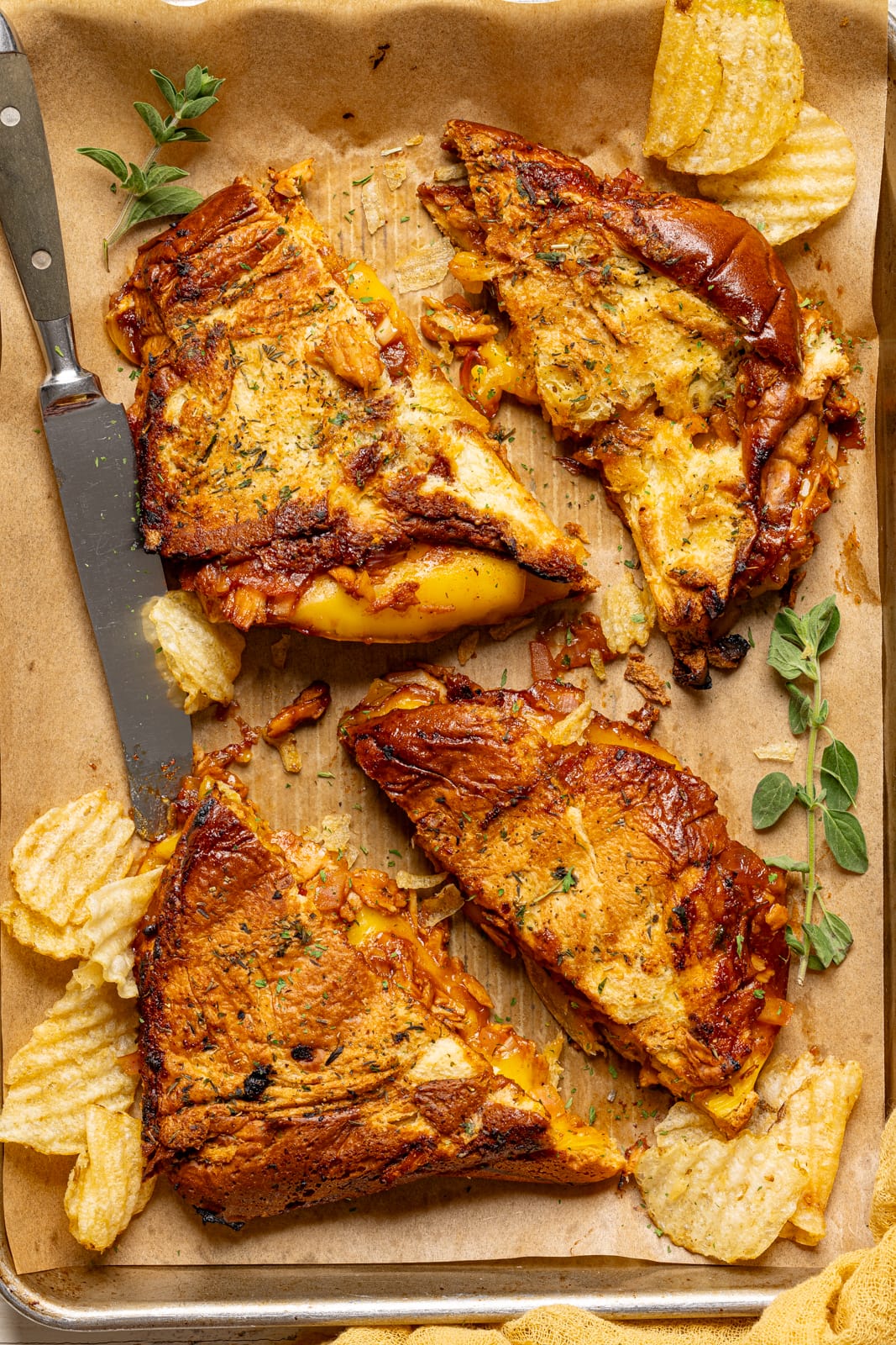 Grilled cheese sandwiches on a baking sheet with parchment paper, a knife, and chips. 