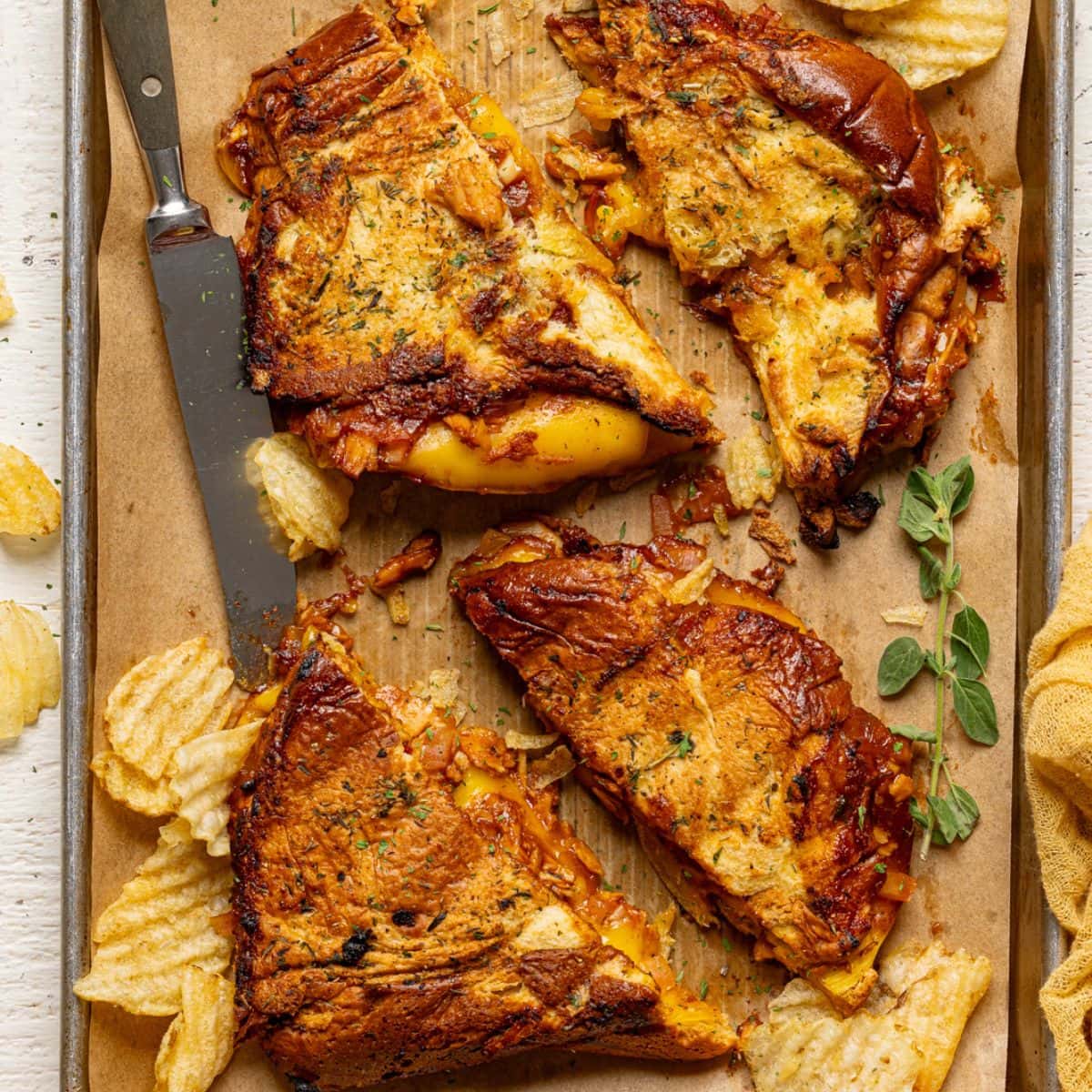 Sandwiches on a baking sheet with parchment paper with a knife and chips.