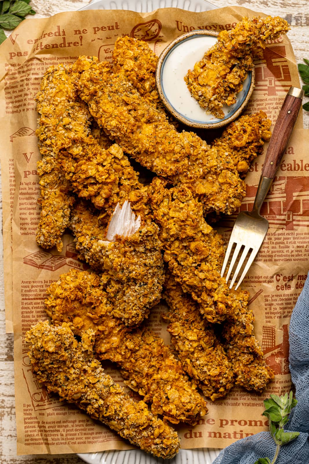 Chicken tenders on a platter with brown paper with a fork and ranch sauce. 