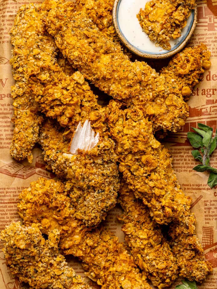 Up close shot of chicken tenders on a platter with brown paper with a fork and ranch sauce.