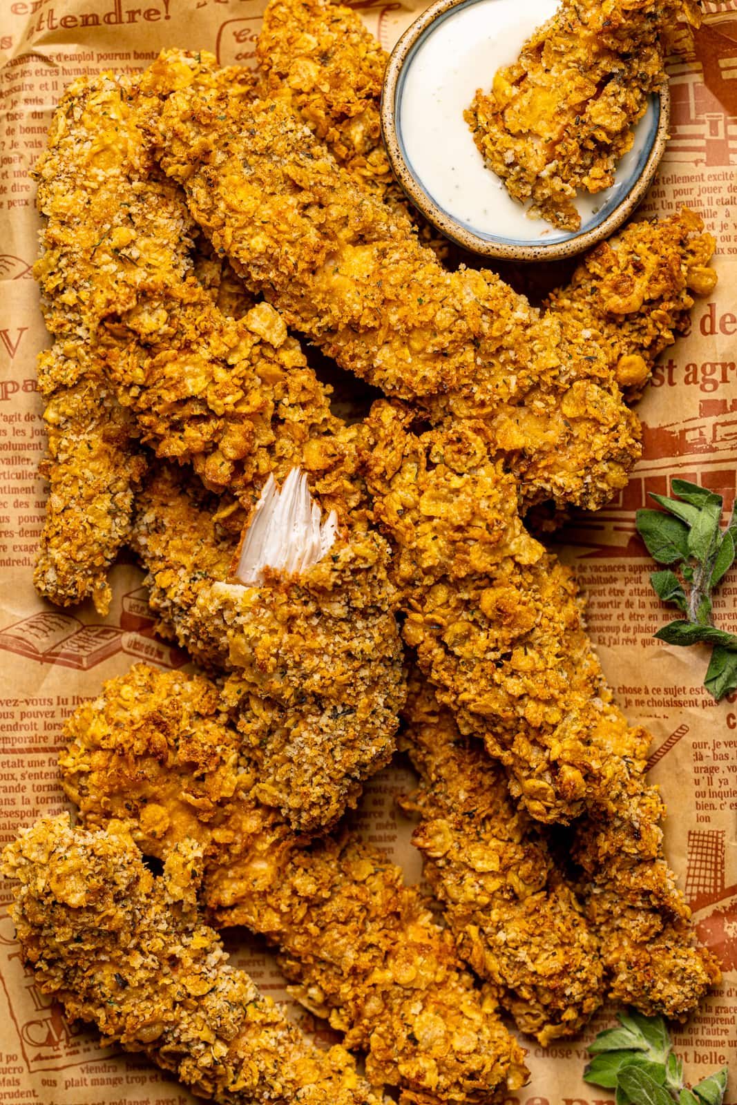 Up close shot of chicken tenders on a platter with brown paper with a fork and ranch sauce.