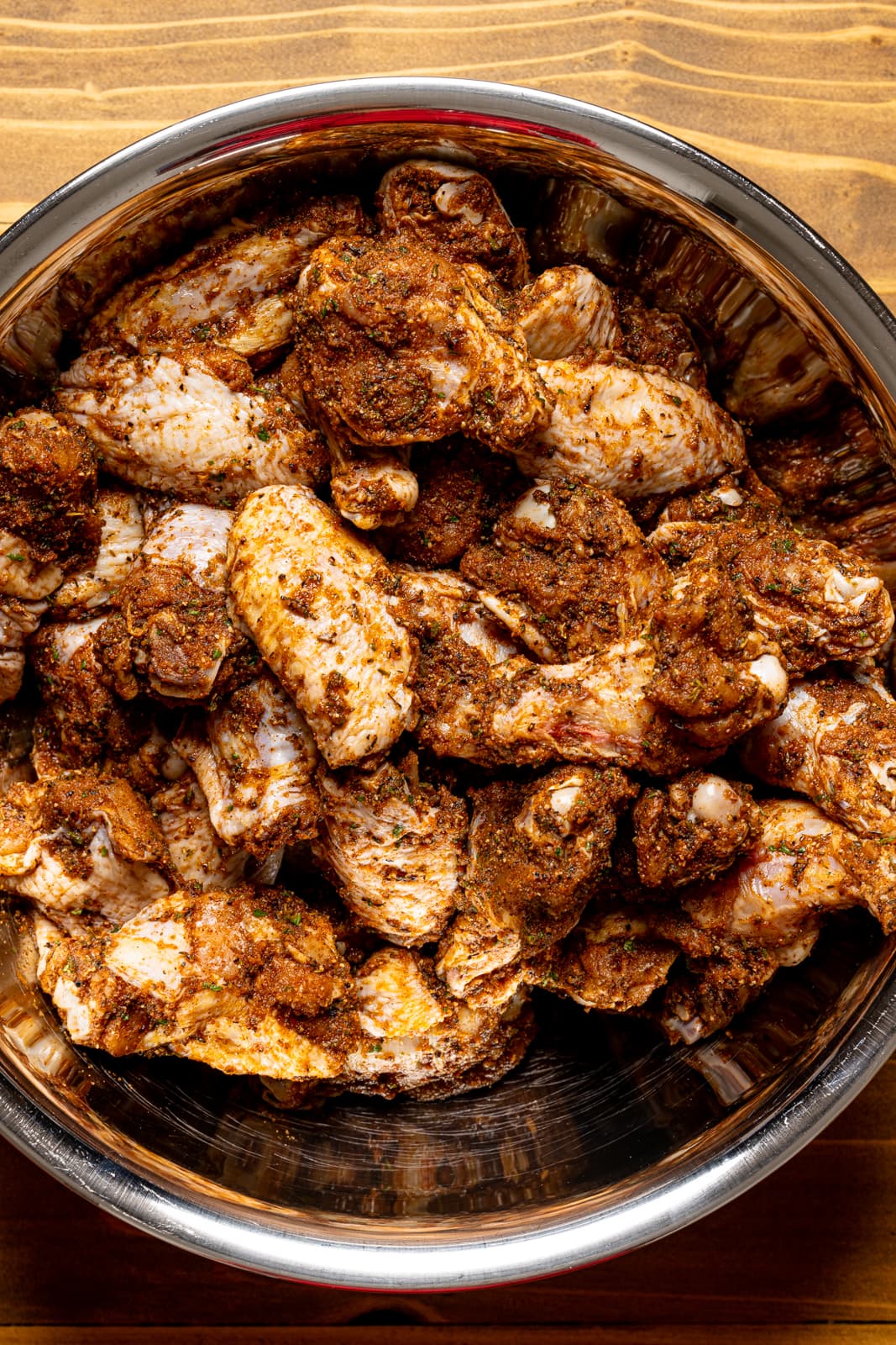 Chicken wings marinated in a large silver bowl on a brown wood table.