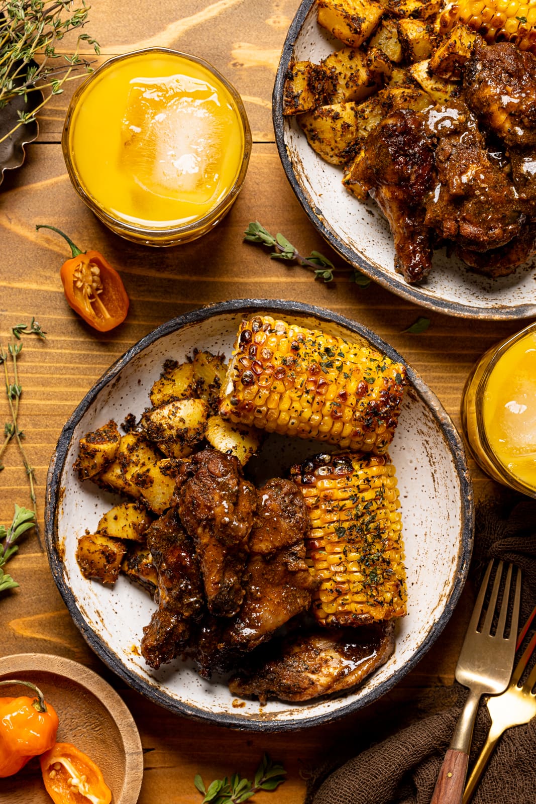 Chicken wings in a bowl with corn and potatoes on a brown wood table with drinks.