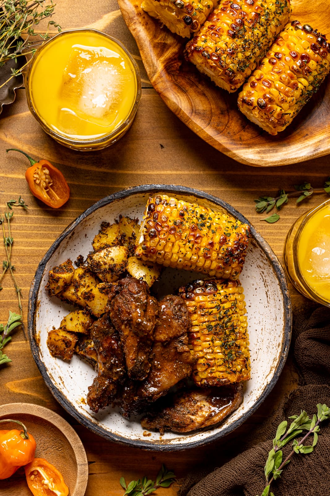 Chicken wings in a bowl with corn and potatoes on a brown wood table with drinks.