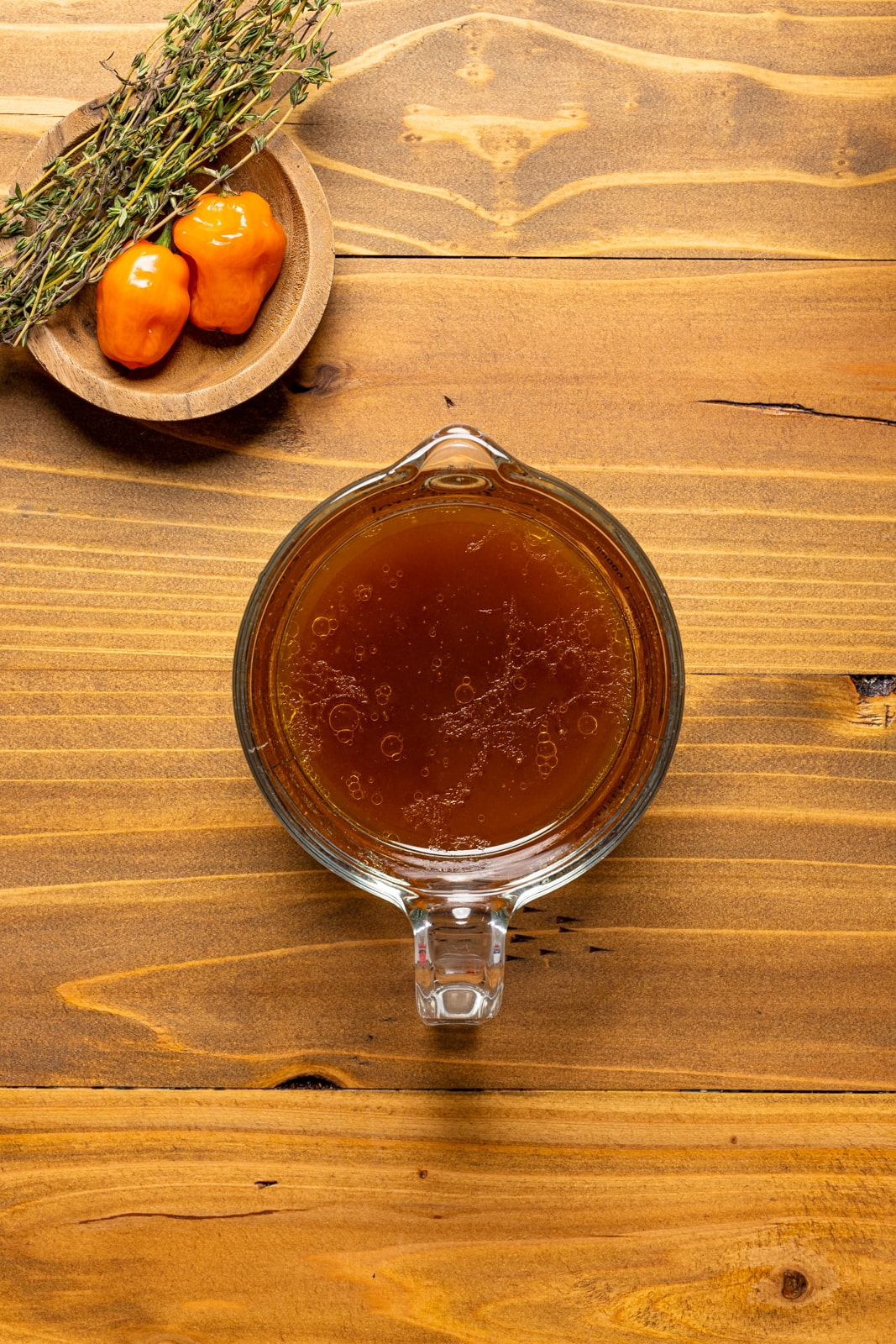 Chicken broth from cooked wings in a measuring cup on a brown wood table.