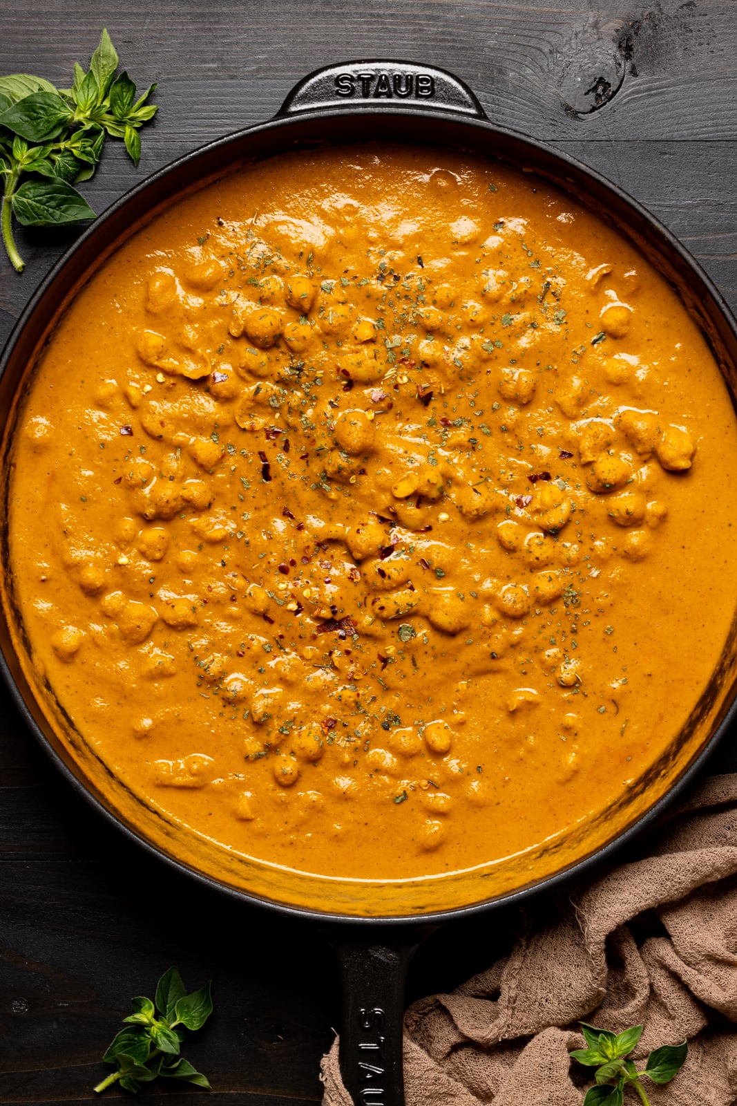 Curry butter chickpeas in a black skillet on a black wood table with brown napkin and herbs.