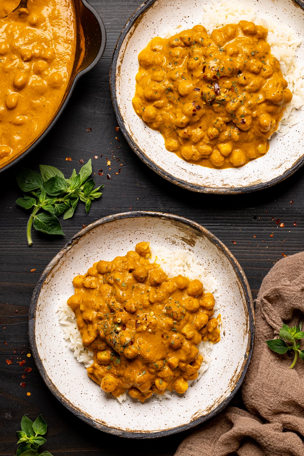 Chickpeas in two low bowls on a black wood table with a brown napkin and herbs.