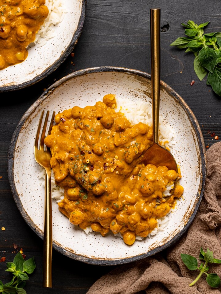 Chickpeas in a low bowl on a black wooden table with a fork and spoon.