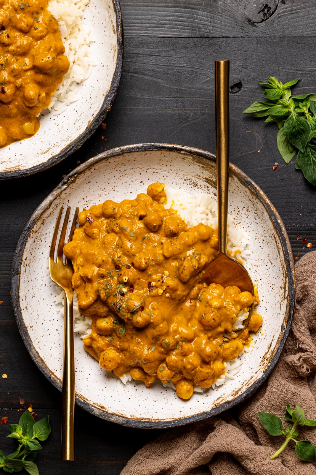 Chickpeas in a low bowl on a black wooden table with a fork and spoon.