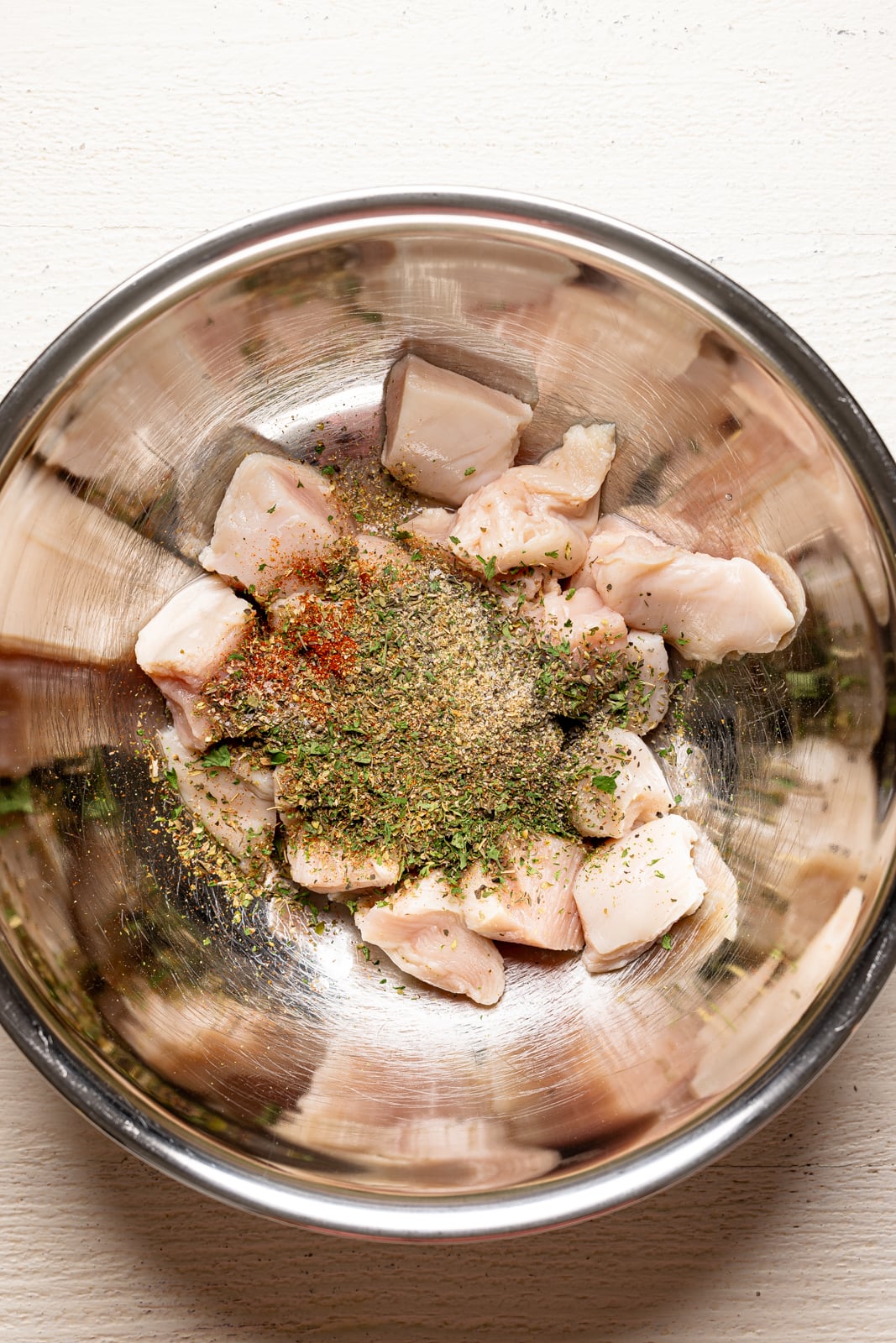 Diced chicken in a large silver bowl with seasonings and herbs. 