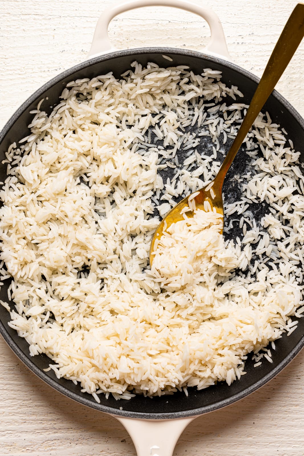 Cooked white rice in a white skillet with a gold spoon.