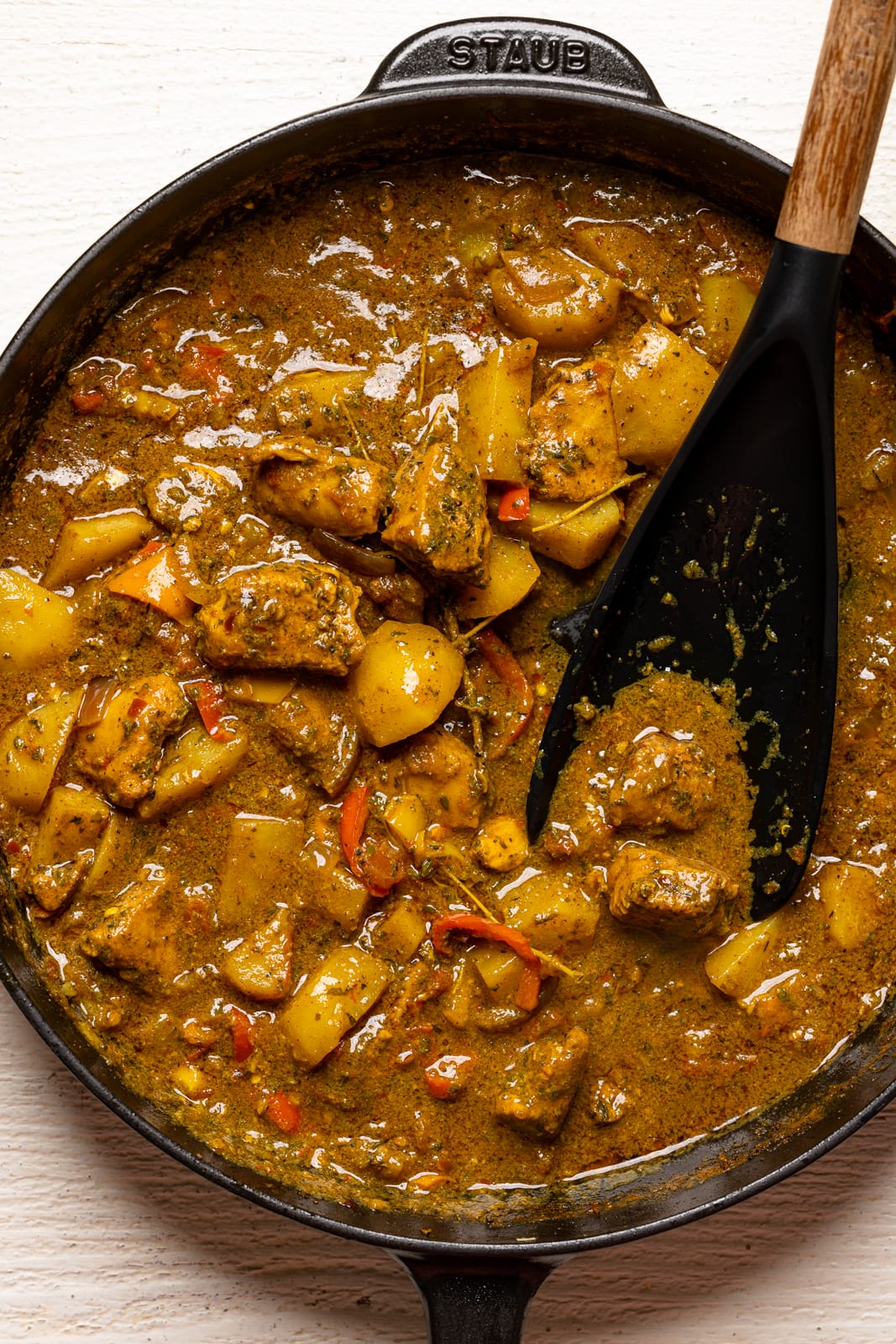 Curry chicken in a black skillet with a spoon on a white table.