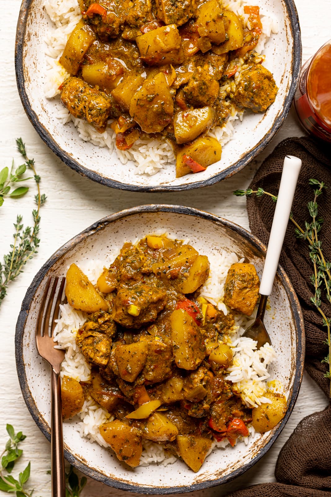 Curry chicken and rice in bowls on a white table with two forks and garnish.