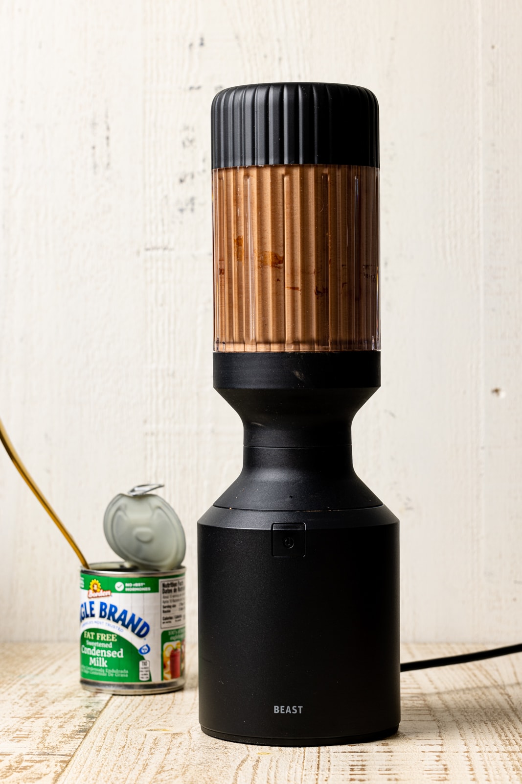 Ice cream mixture in a black blender on a white wood table with an opened can of condensed milk.