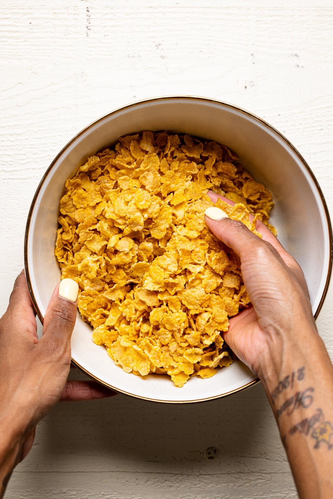 Crushed cornflakes in a white bowl on a white table being held.