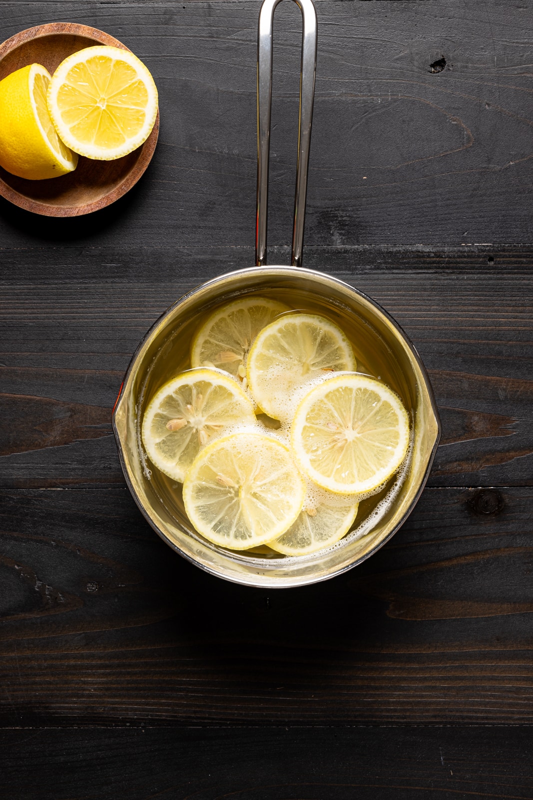 Simple syrup in a saucepan with sliced lemons on a black table. 