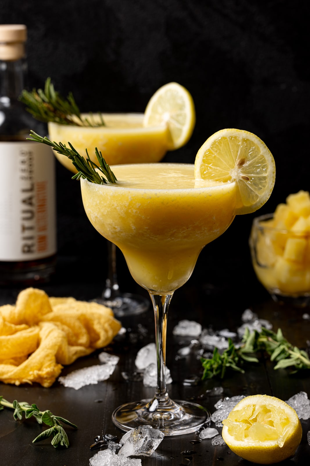 Two glasses of margaritas on a black table with lemons and ice. 