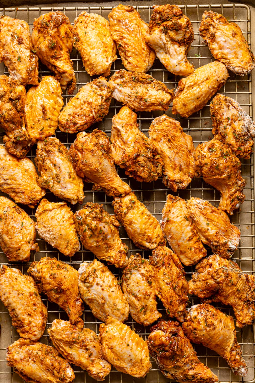 Seasoned chicken wings lined on a baking sheet with a wire rack. 