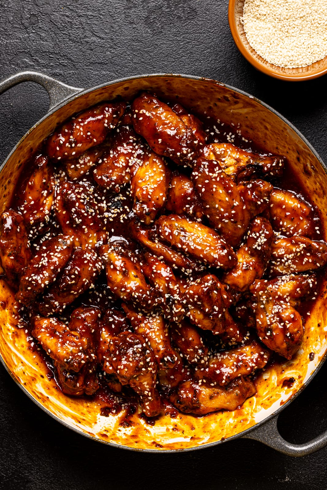 Large dutch oven filled with cooked chicken wings and sesame seeds.