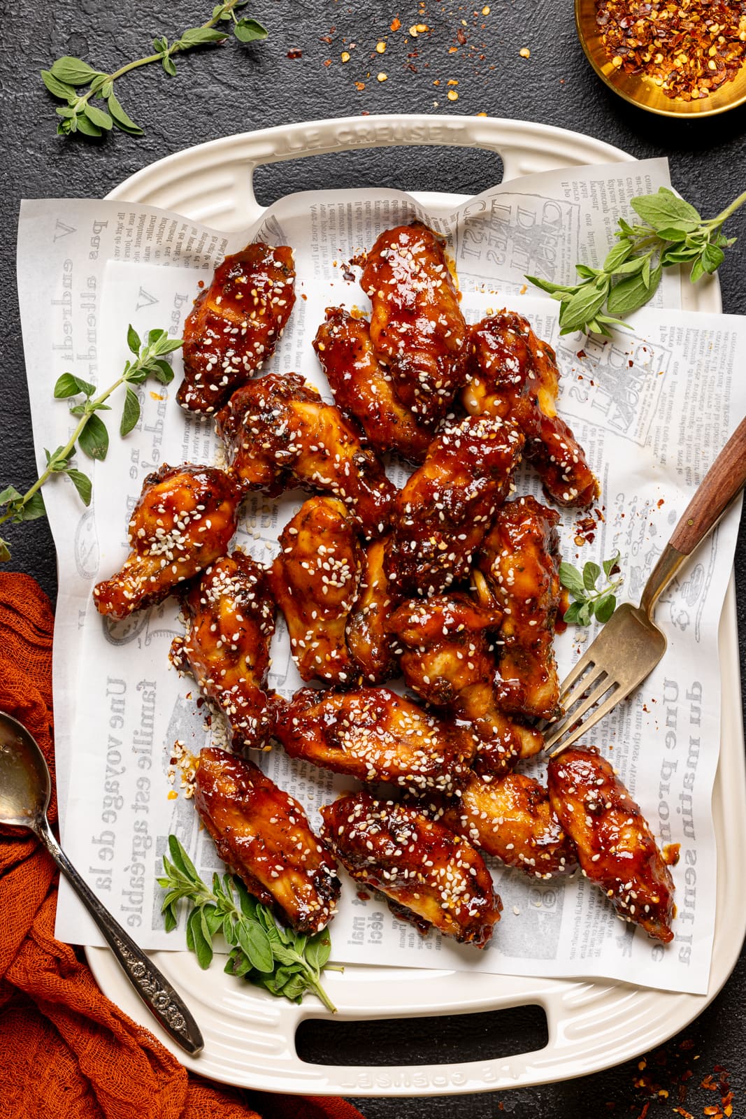 Chicken wings on a platter with white paper and a fork and spoon. 