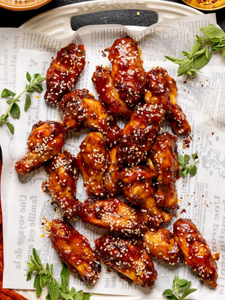 Chicken wings on a platter with white paper, herbs, and sesame seeds.