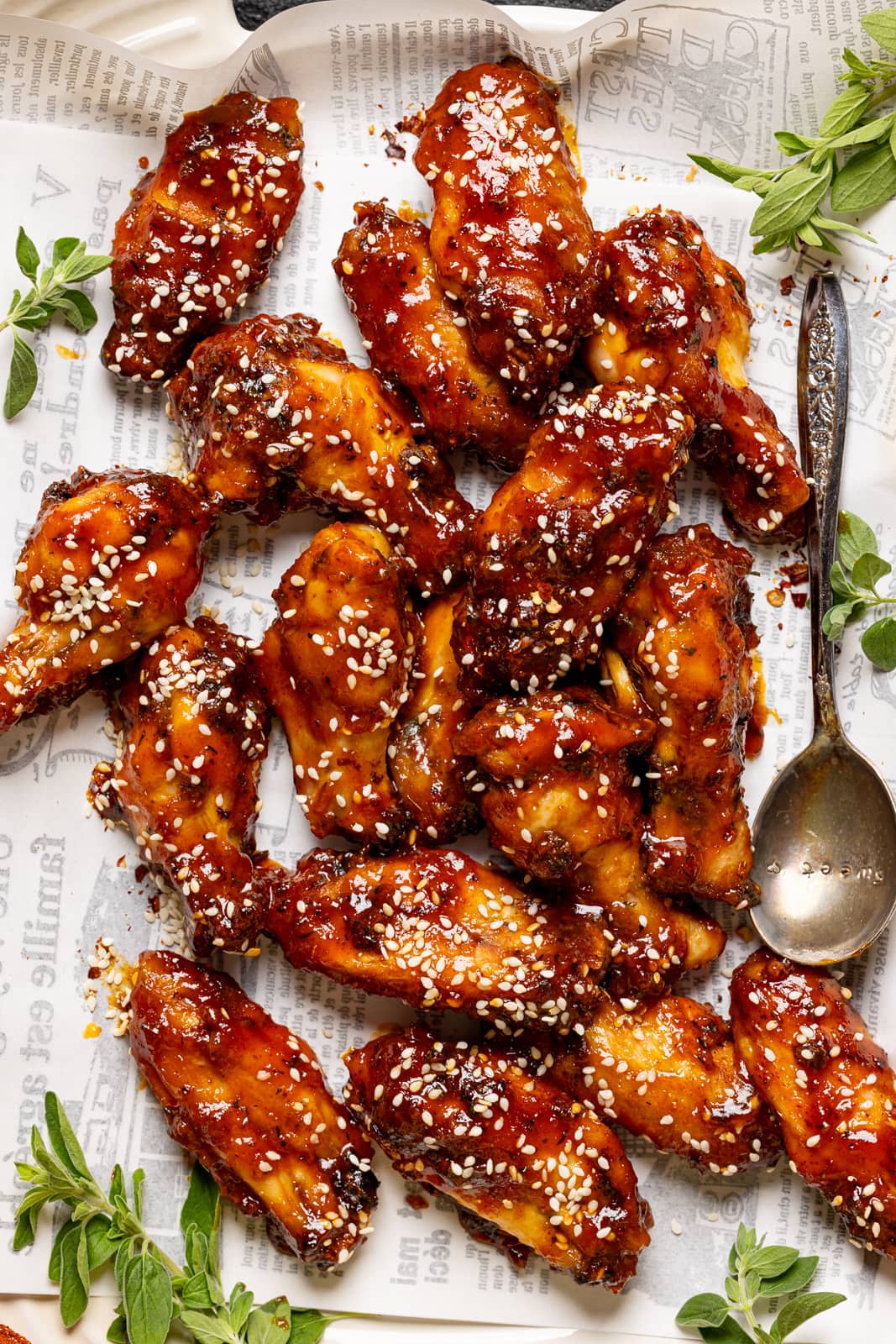 Chicken wings with sesame seeds on white paper with a spoon and garnish. 
