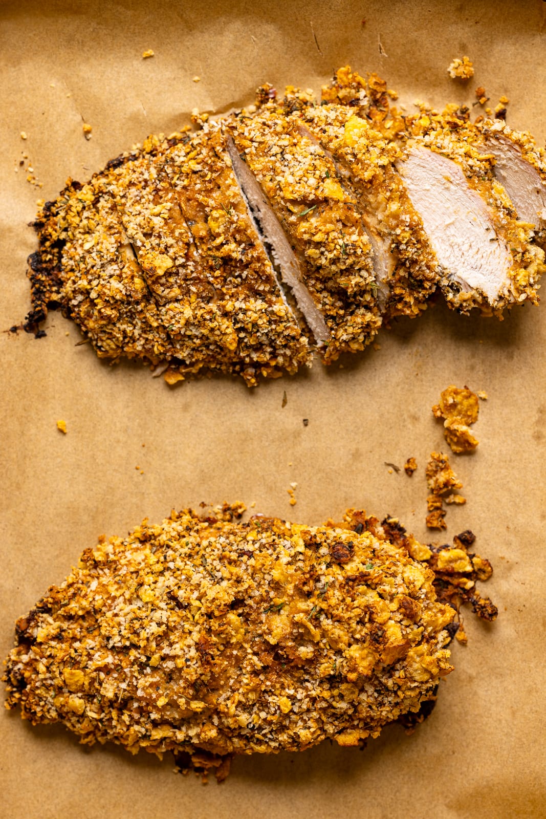 Crusted baked chicken on a baking sheet on a parchment paper. 