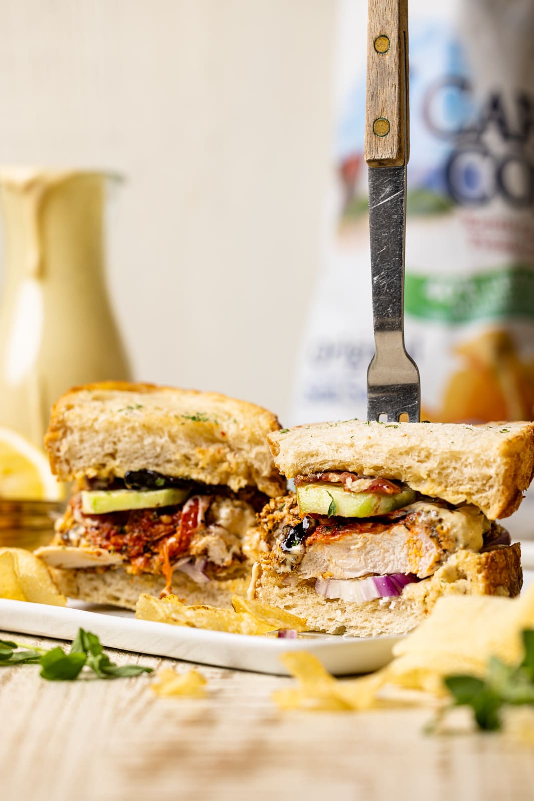 Sandwiches on white plate with a fork and chips and honey mustard in the background.