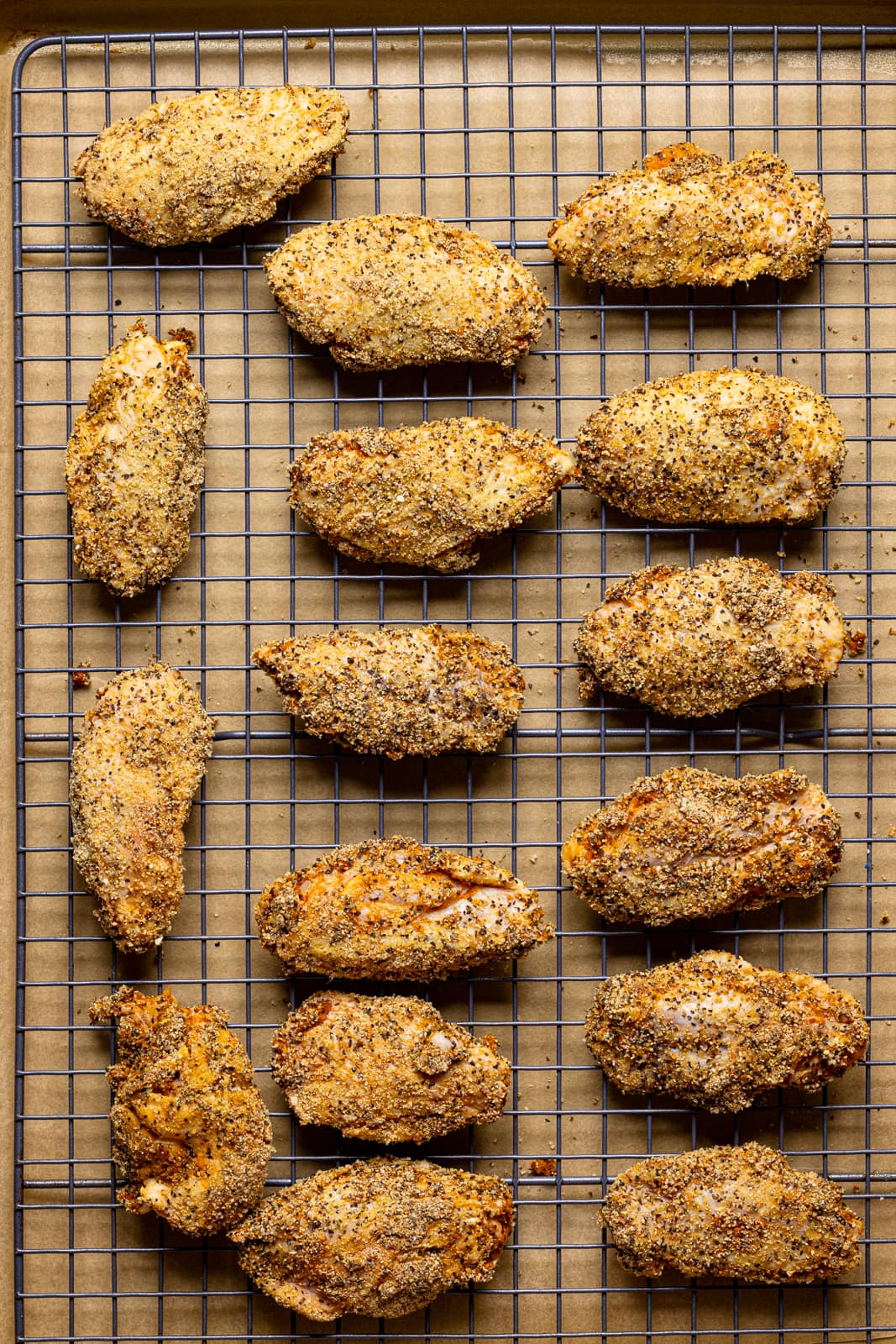 Coated chicken wings on a baking sheet with parchment paper and a wire rack.