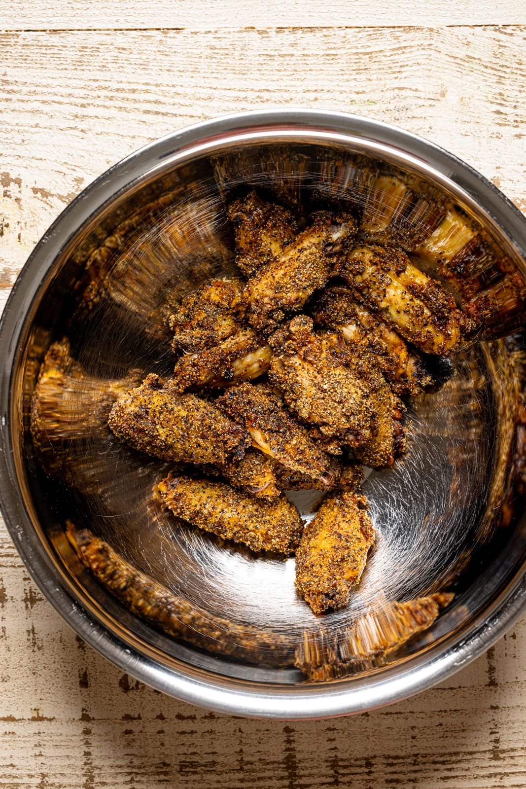 Baked chicken wings in a large silver bowl on a white wood table.