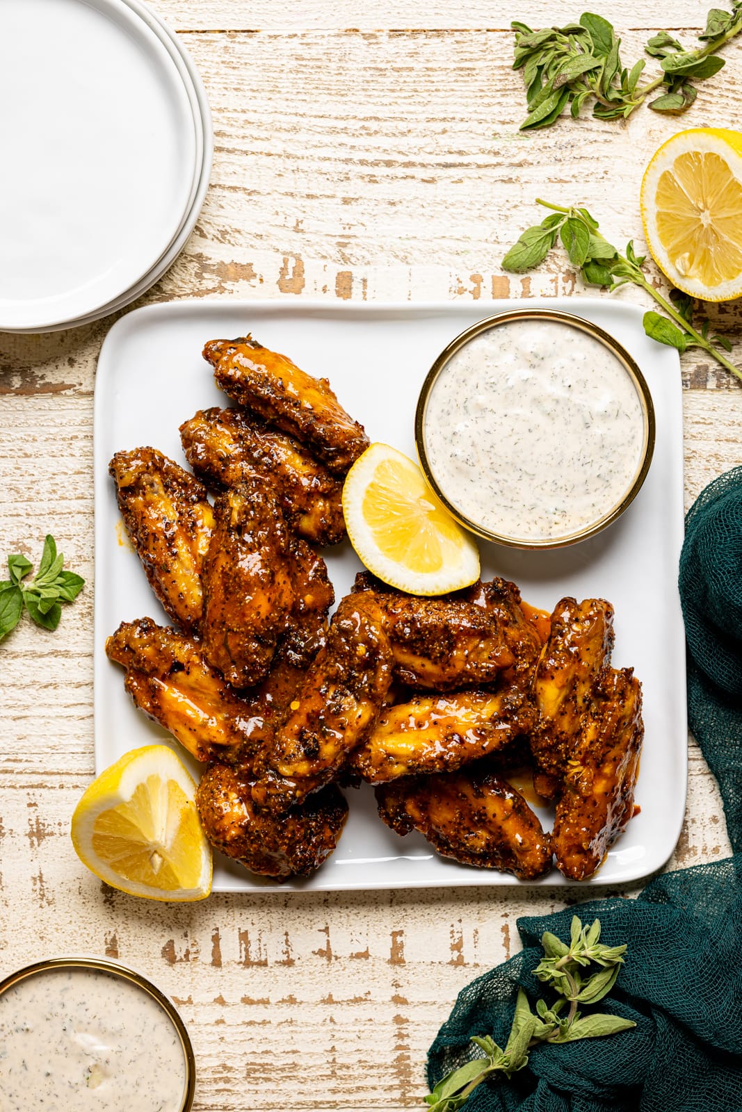 Lemon pepper buffalo wings on a square white plate with dipping sauce, lemon slices, and white plates on the side.