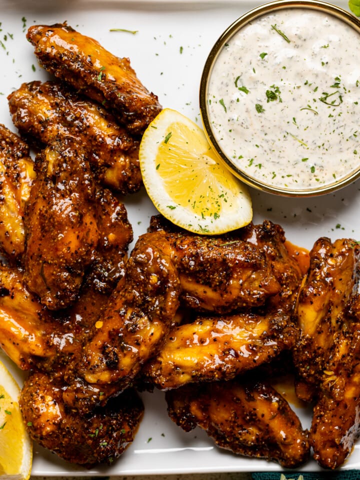 Up close shot of lemon pepper buffalo chicken wings on a white plate with dipping sauce and lemons.