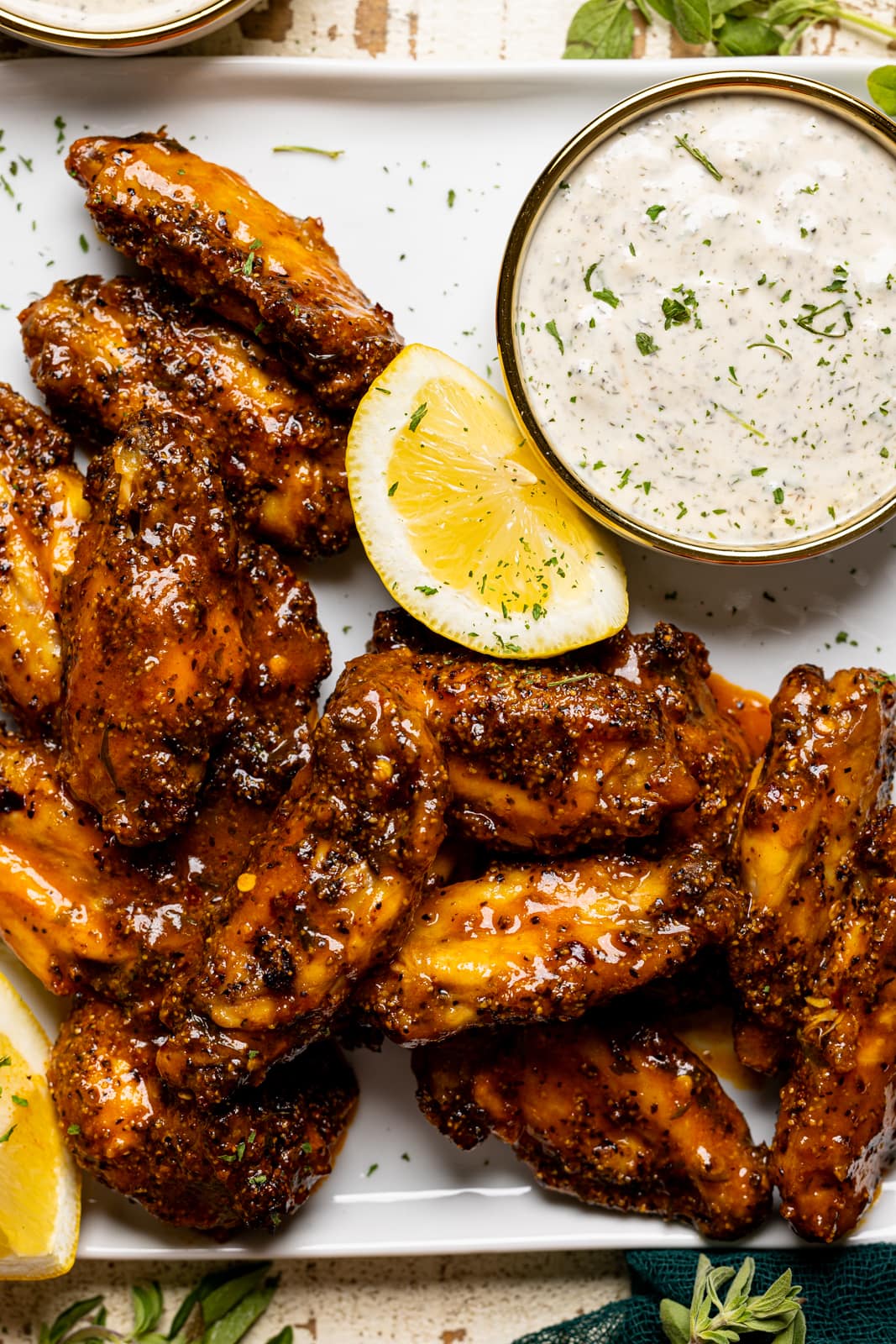Up close shot of lemon pepper buffalo chicken wings on a white plate with dipping sauce and lemons.