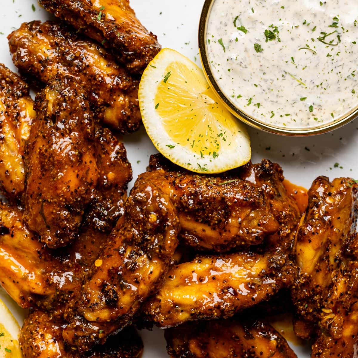 Up close shot of lemon pepper buffalo chicken wings on a white plate with dipping sauce and lemons.