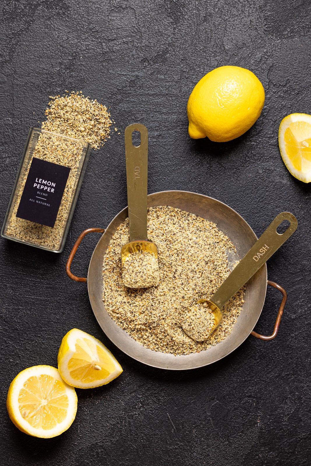 Seasoning in a bowl with two measuring spoons and lemons on a black table.