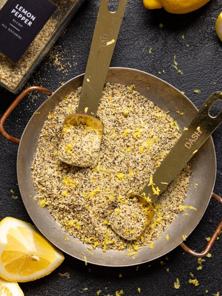 Seasoning in a bowl with two measuring spoons, lemons, and jar on a black table.
