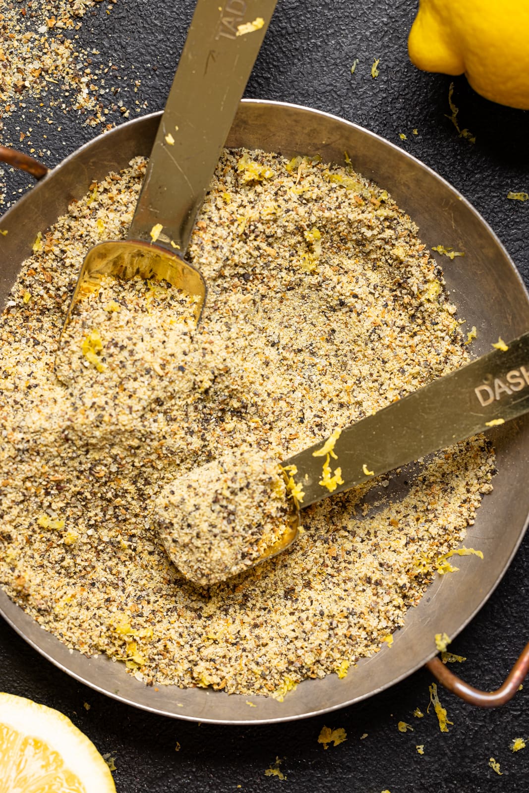 Lemon pepper seasoning in a bowl with measuring spoons and lemons. Homemade seasoning.