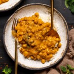 Chickpeas in a low bowl on a black wood table with a fork and knife.