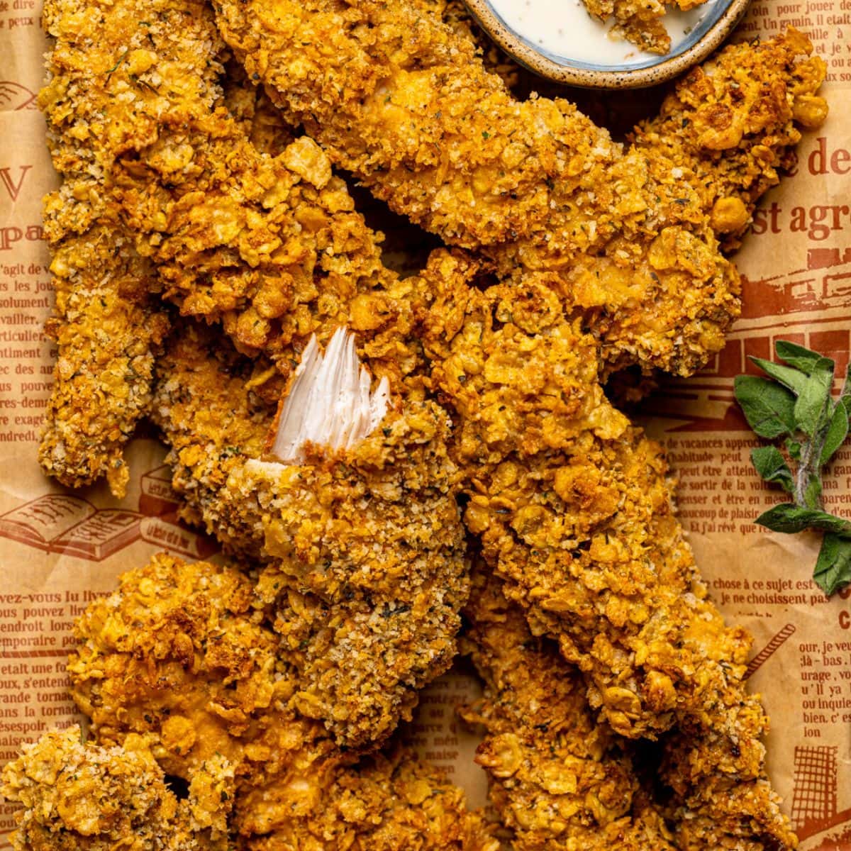 Up close shot of Chicken tenders on a platter with brown paper with a fork and ranch sauce.