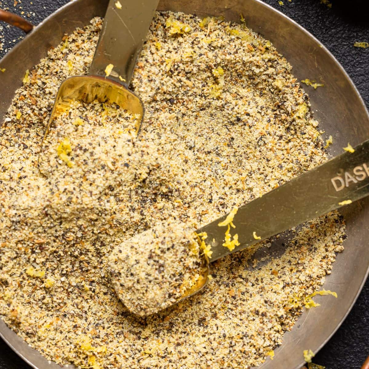 Lemon pepper seasoning in a bowl with measuring spoons and lemons.