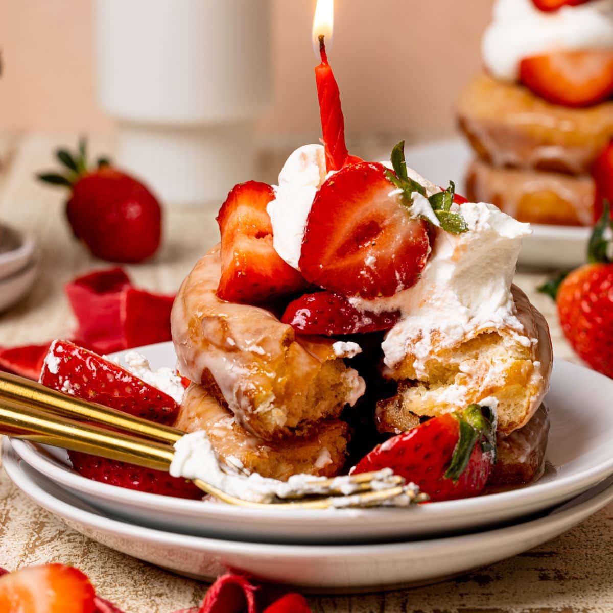 Red candle in a stack of strawberry shortcake donuts on white plates.