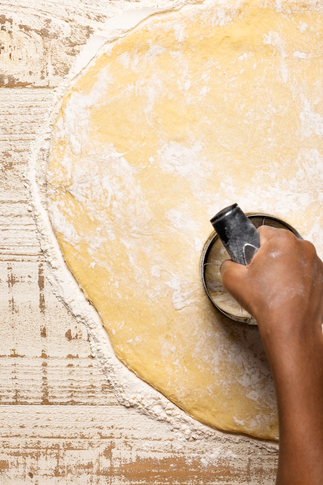 Rolled out donut dough on a white wood table with a doughnut cutter.