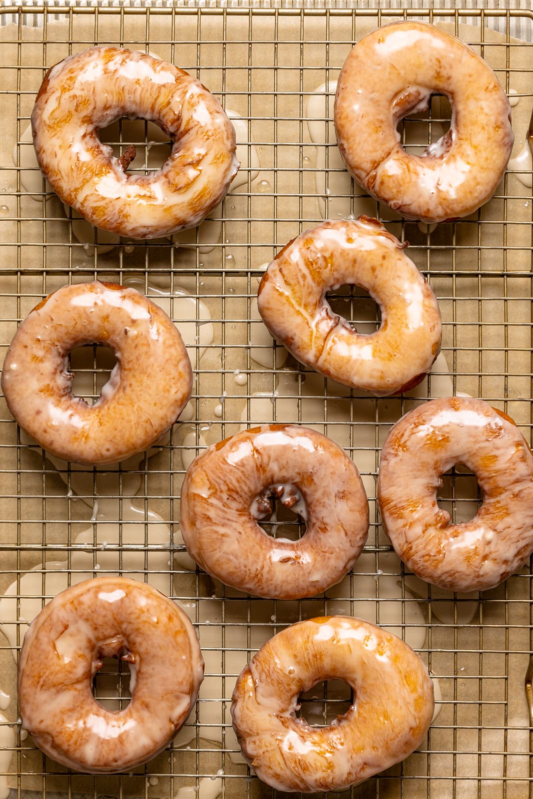 Baked glazed donuts on a baking sheet with a wire rack.