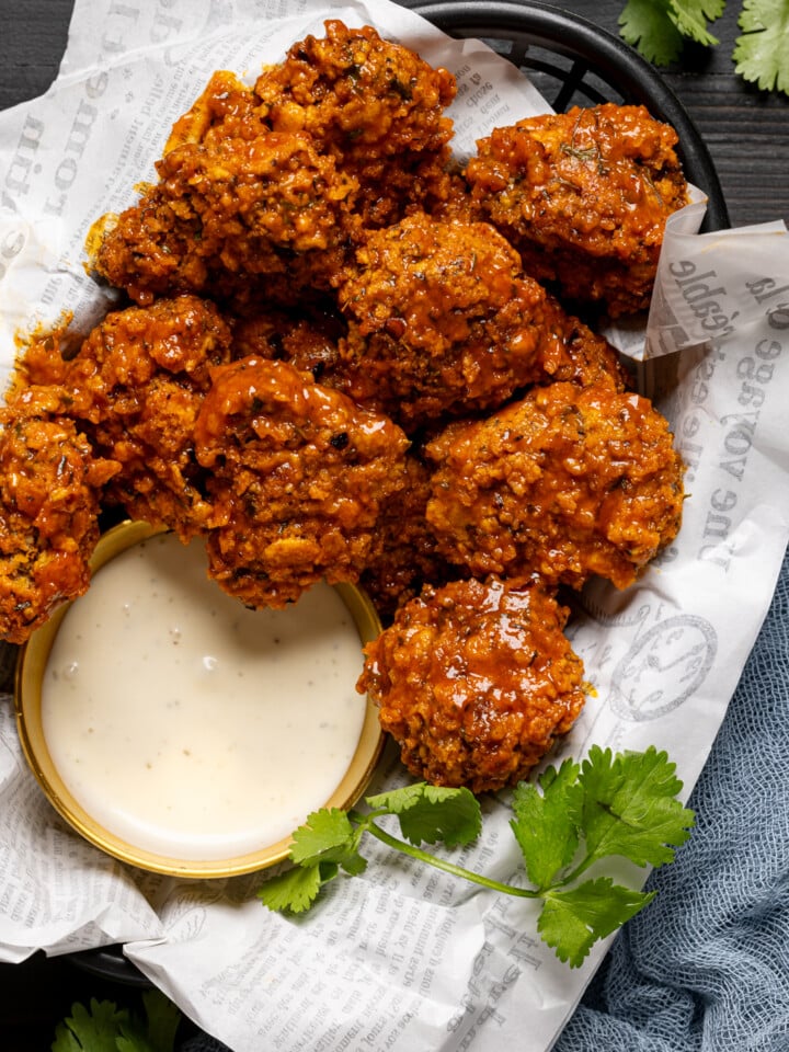 Up close shot of chicken in a basket with dipping sauce and fresh herbs.